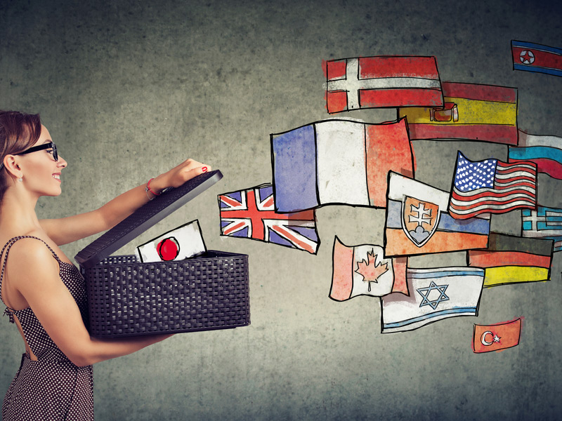 Frau öffnet Koffer, aus dem gezeichnete Landesflaggen verschiedener Länder schweben.