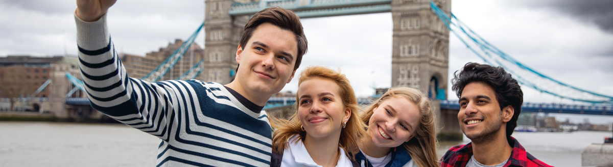 Vier junge Erwachsene machen ein Selfie vor der Tower Bridge in London.