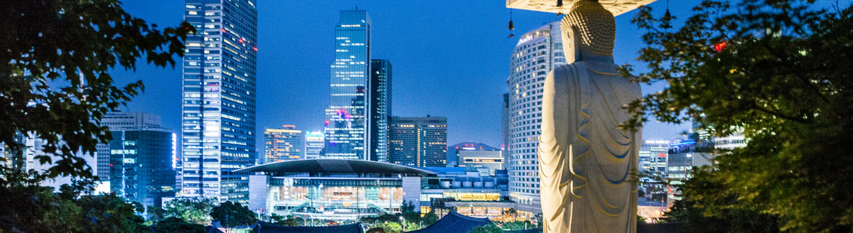 Blick über Seoul bei Nacht mit moderner Skyline und großer Buddha-Statue – Sprachreise nach Südkorea