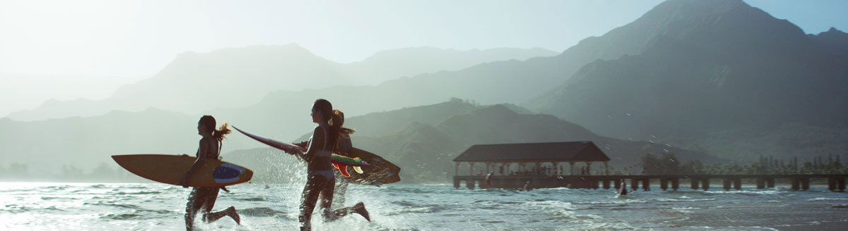 Surferinnen im Meer vor beeindruckender Bergkulisse bei einer Englisch-Sprachreise in den USA